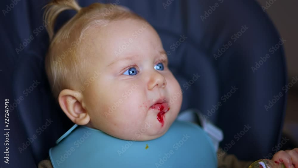 Face of a cute chubby Caucasian baby with food on his chin. Close up. Kid takes a spoon from his mom and pulls it to his mouth. Face of a cute chubby Caucasian baby with food on his chin. Close up. Kid takes a spoon from his mom and pulls it to his mouth.