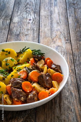 Roast pork cheeks with carrots and celeriac in sauce with boiled potatoes on wooden table  photo