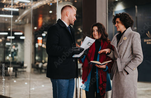 Young professionals engage in a lively discussion outside an office building, with paperwork and a digital tablet in hand.