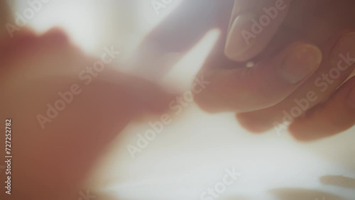 Against the backdrop of the cozy morning light, a mother tenderly touches her newborn's little feet. Her gentle hands carefully hug the baby's arms, filling the room with incredible warmth and love photo