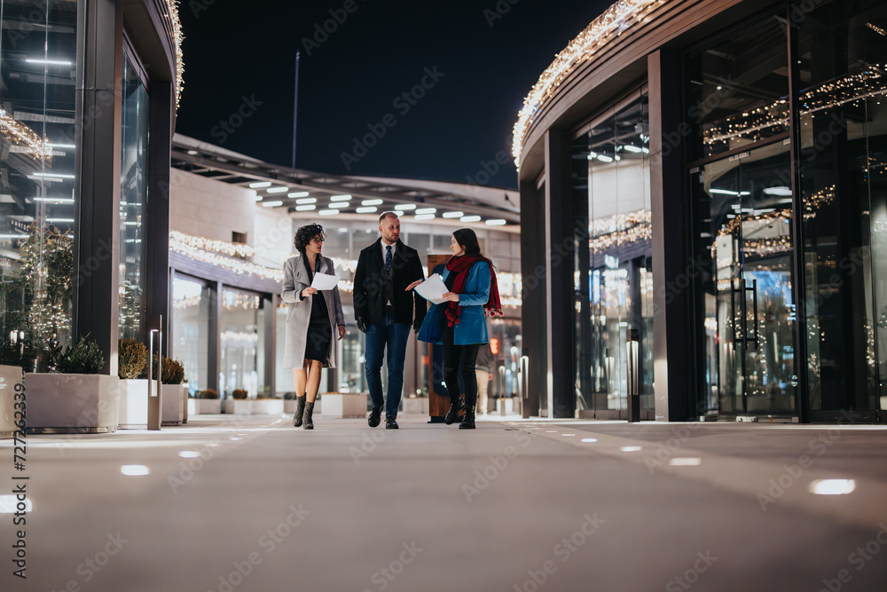 Young professionals in business attire walk and converse outside an office building adorned with festive lights, creating a blend of corporate and holiday vibes..