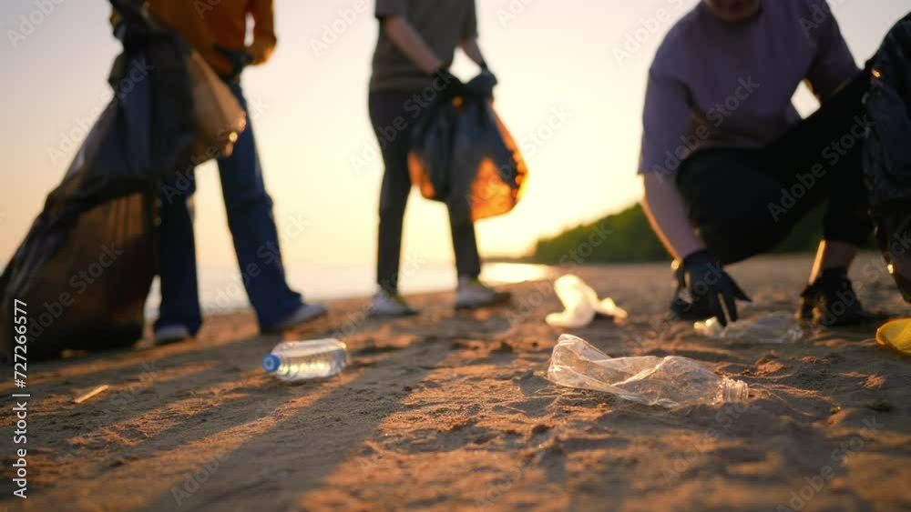 Volunteers guys collecting trash garbage and sorting in bags on sea coast at sunset. Environment pollution protection. Put on trash, rubbish, junk in plastic pockets, volunteering concept. Blur video.
