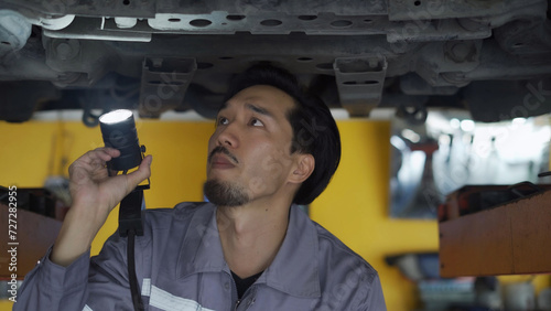 The mechanic walks under the raised car and the maintenance technician inspects the car and performs diagnostic repairs.