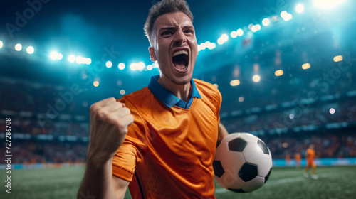 excited soccer player in an orange jersey is holding a soccer ball, celebrating with a stadium in the background
