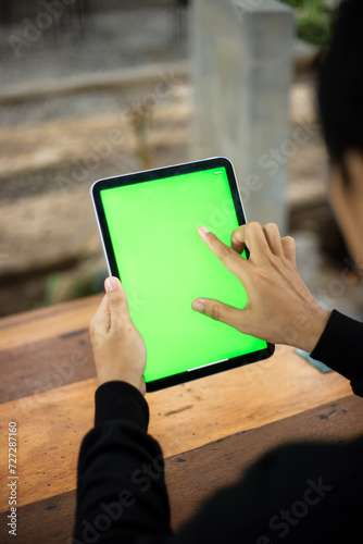 Mock up photo of a close up shot featuring a mans hand holding an iPad tablet with a green screen against the background of a wood cafe table