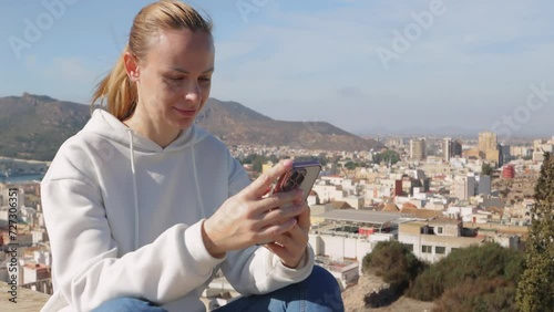 happy tourist girl sitting, admiring the view of the city from above, holding the phone in her hands photo