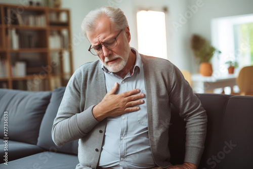 Elderly man having heart attack and acute pain sitting on sofa in living room photo