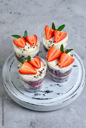Chocolate biscuit trifles with cherry filling. Dessert is decorated with cream cheese cream, fresh strawberries, chocolate balls and green leaves.