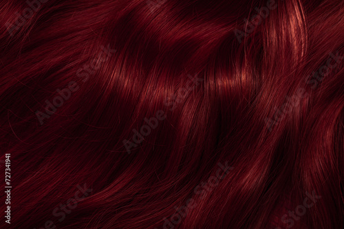 Dark red hair close-up as a background. Women's long brown hair. Beautifully styled wavy shiny curls. Coloring hair with bright shades. Hairdressing procedures, extension.