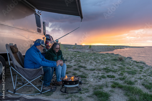 Matured Caucasian couple warming their hands by a campfire sitting under an awning by a lake at sunset, Big Sandy Reservoir, Wyoming