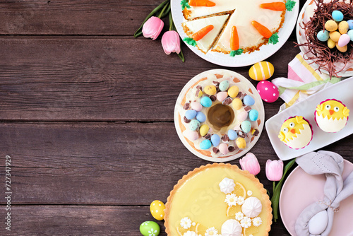 Easter or spring dessert food side border. Above view over a dark wood background. Lemon tart, cupcakes, Easter egg and carrot cakes and a collection of sweets. Copy space.