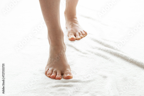 The bare feet of a young girl stand on a white carpet at home in an apartment in the light, feet