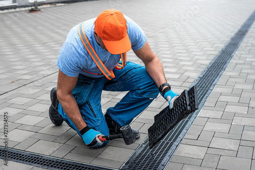 Laying interlocking paving. A worker is placing the grutter grid to drainage channel.