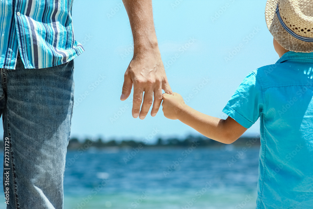 A happy dad holds the hand of a child by the greek sea in nature A happy dad holds the hand of a child by the greek sea in nature