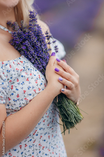 A girl stands in a field of lavender and holds a bouquet in her hands