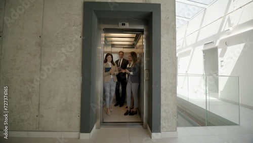 Four colleagues step out of an elevator into a sunlit atrium, signaling the start of a productive workday in a modern office environment