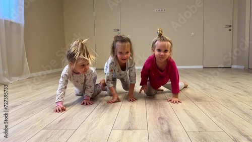 Three little sisters triplets crawl around the room at home in pajamas with bare feet, the room  photo