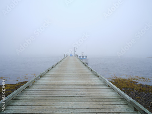 Lobster and fishing boat docked on a long wooden dock in mist and fog