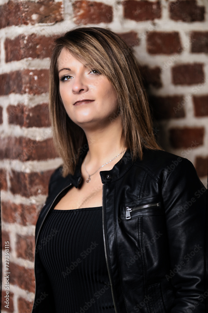 Woman model around thirty in black leather jacket and hot pants in front of urban brick wall. Woman model around thirty in black leather jacket and hot pants in front of urban brick wall.