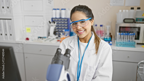 Smiling young hispanic woman scientist with microscope in the laboratory