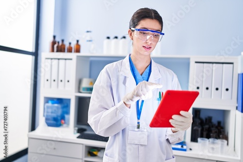 Young beautiful hispanic woman scientist using touchpad at laboratory photo