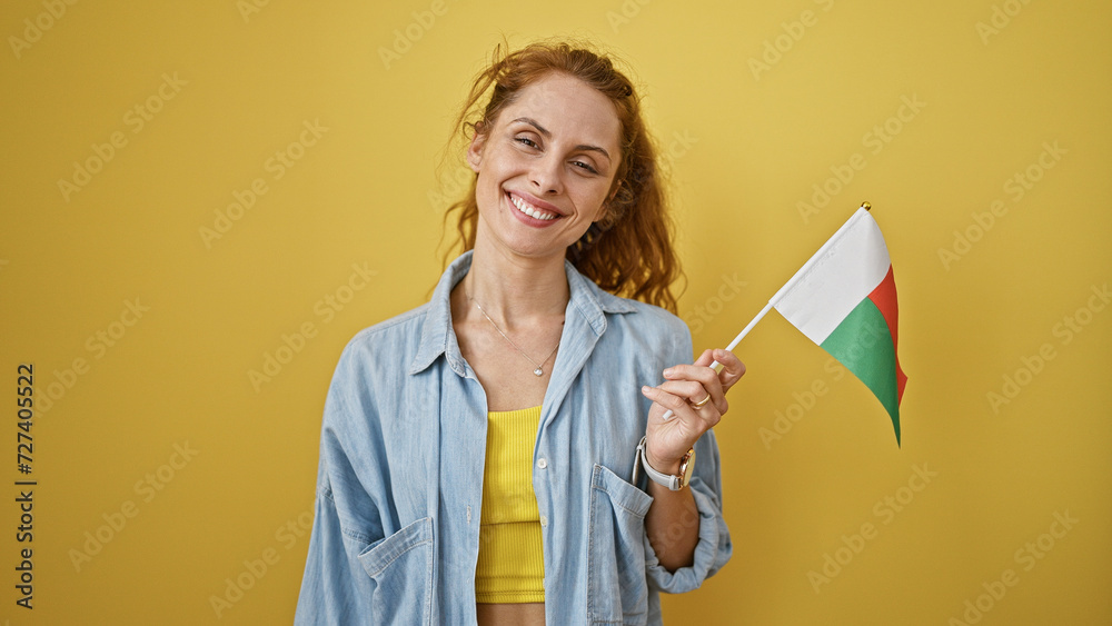 A smiling young woman holding the madagascar flag against a vibrant yellow background - obrazy, fototapety, plakaty 
