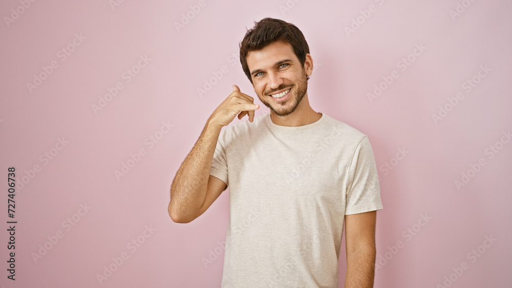 Smiling young hispanic man with beard making call me gesture against a pink isolated background Smiling young hispanic man with beard making call me gesture against a pink isolated background