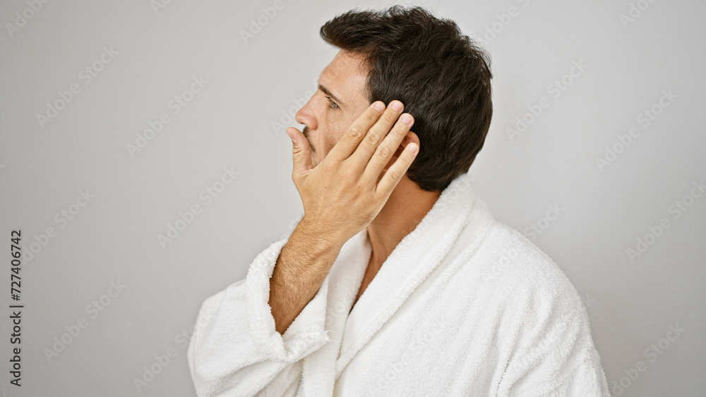 Handsome hispanic man in white bathrobe touching his face against an isolated light background. Handsome hispanic man in white bathrobe touching his face against an isolated light background.