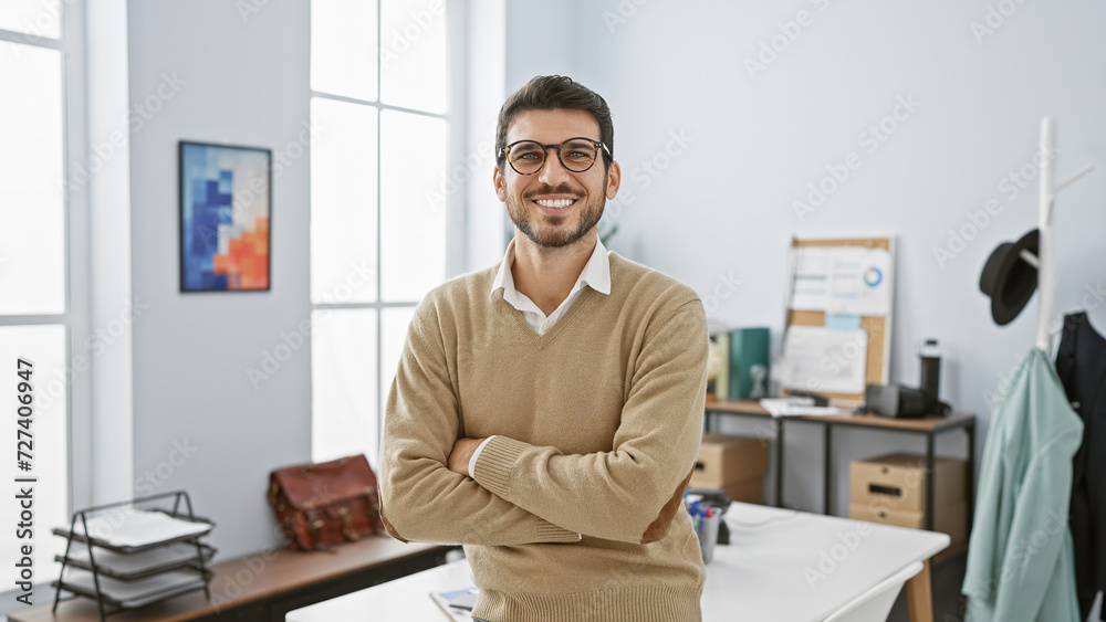 Handsome young man with arms crossed standing confidently in a well-lit modern office interior. Handsome young man with arms crossed standing confidently in a well-lit modern office interior.