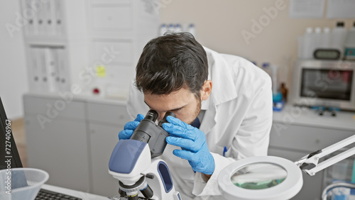 Hispanic man using microscope in laboratory setting  reflecting concentration and scientific research.