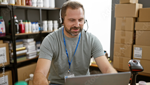 A handsome mature man with grey hair works in a warehouse, surrounded by donations and packages, sporting a headset and a badge. photo
