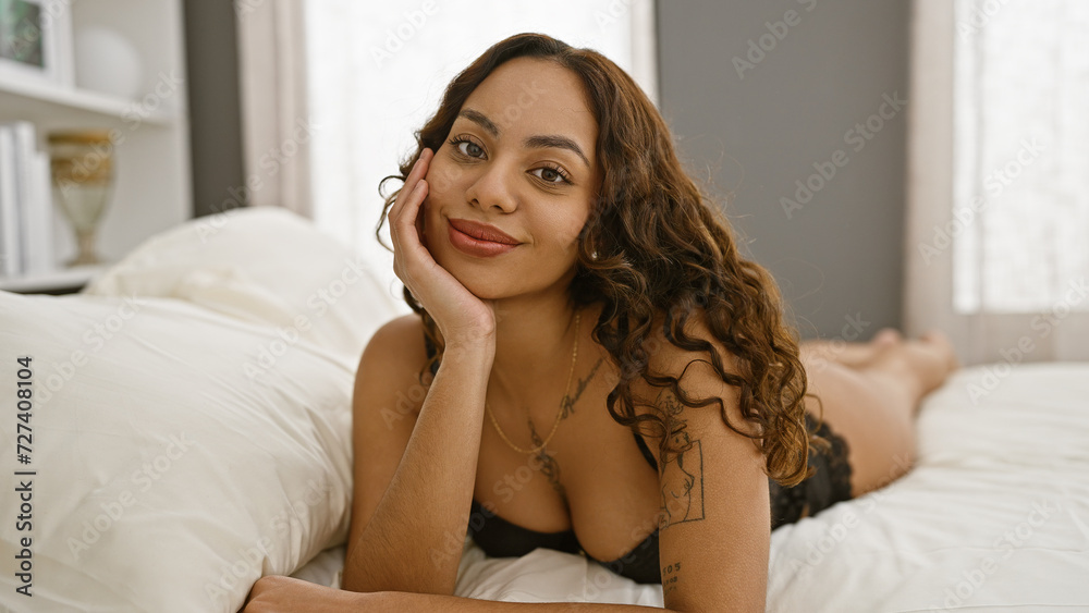 A relaxed young woman posing with a smile in a well-lit bedroom, exuding comforting homeliness and modern femininity.