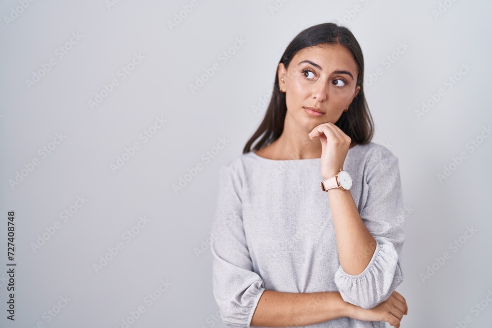 Young hispanic woman standing over white background with hand on chin thinking about question, pensive expression. smiling with thoughtful face. doubt concept. Young hispanic woman standing over white background with hand on chin thinking about question, pensive expression. smiling with thoughtful face. doubt concept.