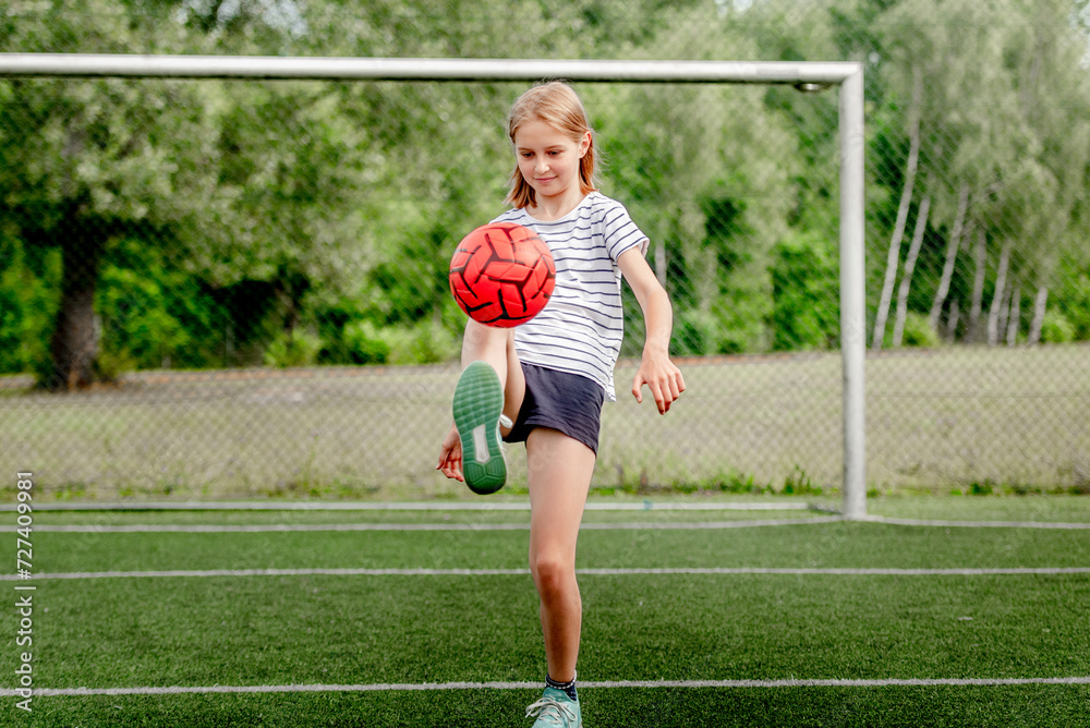 Pretty child girl kicking football ball at socket field. Cute female kid playing active game