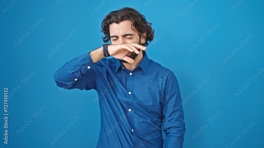 Young hispanic man sneezing over isolated blue background Young hispanic man sneezing over isolated blue background