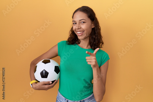 Young hispanic woman holding ball pointing fingers to camera with happy and funny face. good energy and vibes. © Krakenimages.com