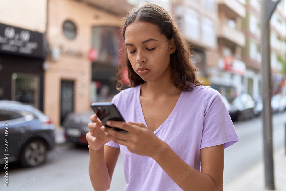Young african american woman using smartphone with serious expression at street