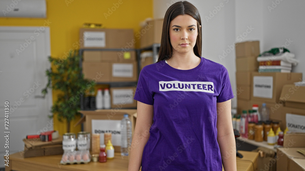 Young beautiful hispanic woman volunteer standing with serious face at charity center Young beautiful hispanic woman volunteer standing with serious face at charity center