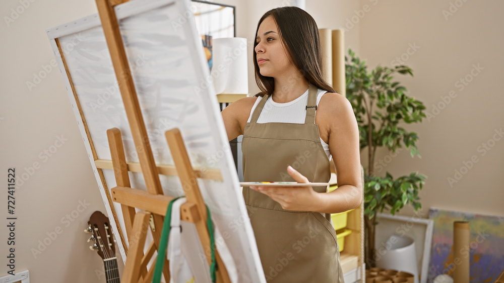 Artistic passion unleashed, young, beautiful hispanic woman artist delightfully drawing at hip art studio, standing clad in apron, palette in hand. Artistic passion unleashed, young, beautiful hispanic woman artist delightfully drawing at hip art studio, standing clad in apron, palette in hand.