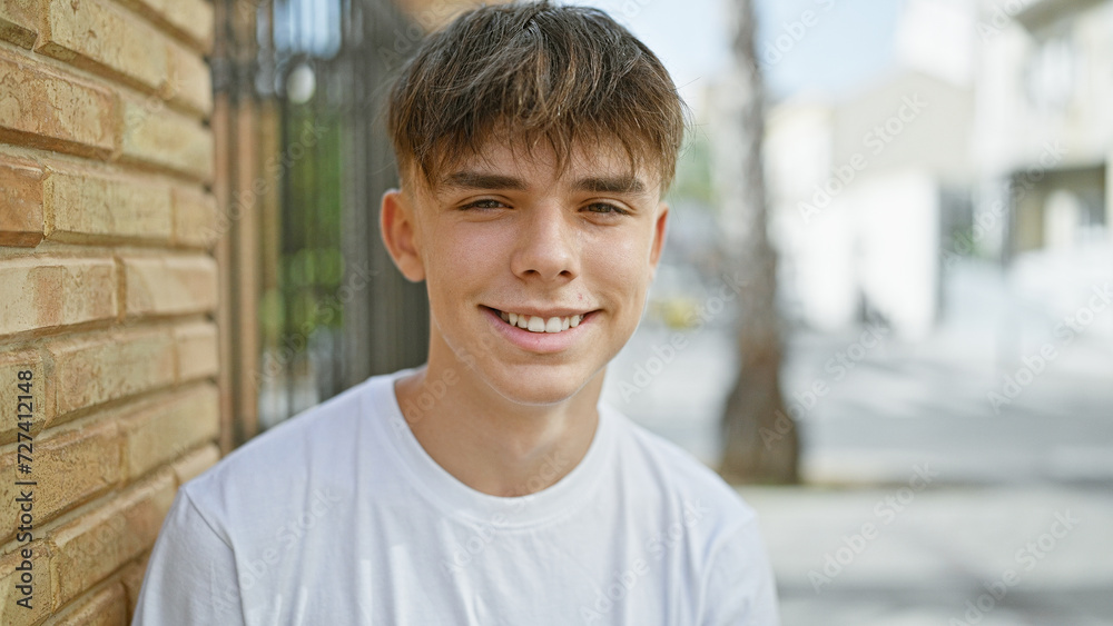 A smiling, blond teen boy outdoors in an urban street setting, posing for a portrait. A smiling, blond teen boy outdoors in an urban street setting, posing for a portrait.