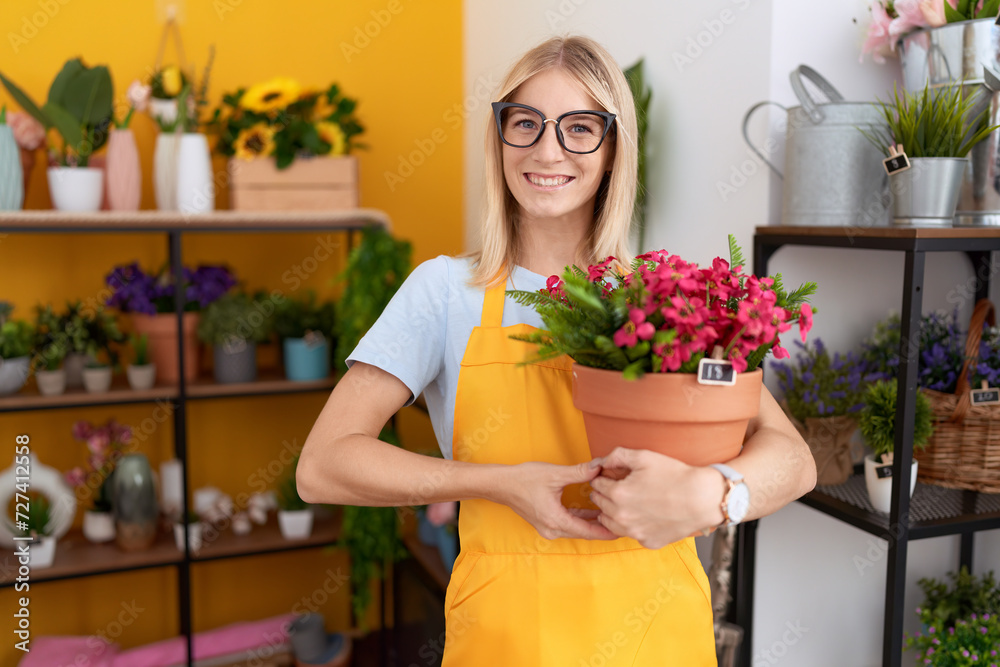 Young caucasian woman working at florist shop holding plant looking positive and happy standing and smiling with a confident smile showing teeth