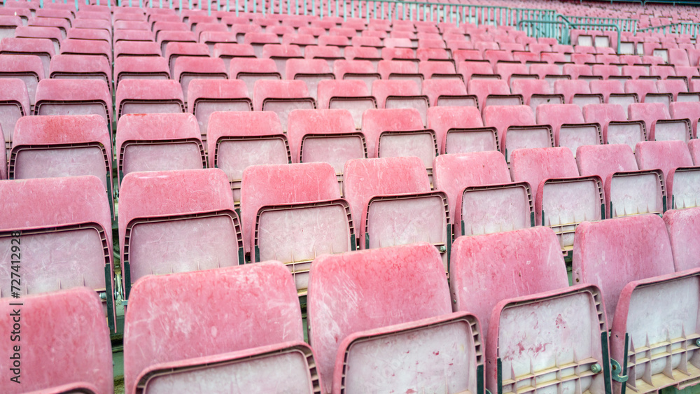 Fototapeta premium Empty and weathered worn down stadium seating in lightened red and pink tones after year of exposure to weather outdoors in daylight. background graphic design resource