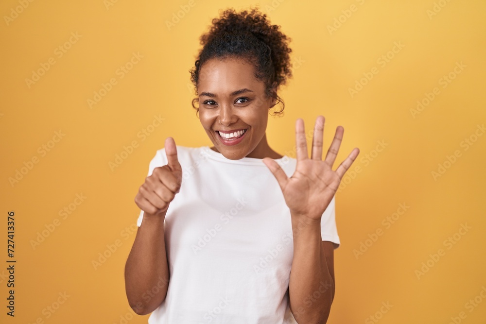 Young hispanic woman with curly hair standing over yellow background showing and pointing up with fingers number six while smiling confident and happy. Young hispanic woman with curly hair standing over yellow background showing and pointing up with fingers number six while smiling confident and happy.