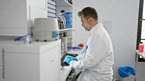 Concentrated young, grey-haired hispanic man, a dedicated scientist, working hard on his computer deep in serious research at his indoor laboratory.