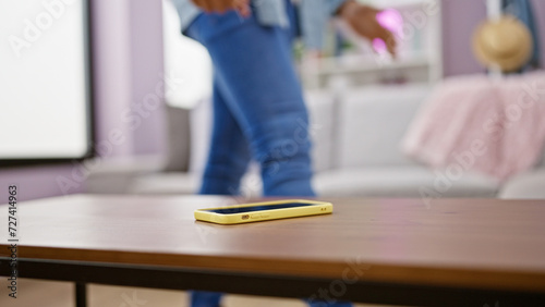 Blurred young man walking away from smartphone on coffee table in a modern living room interior.