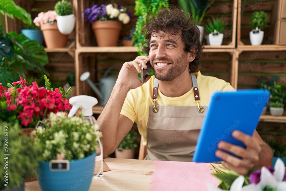Young hispanic man florist talking on smartphone using touchpad at flower shop Young hispanic man florist talking on smartphone using touchpad at flower shop