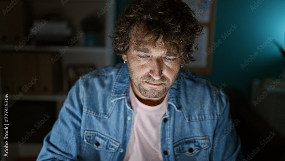 Fototapeta premium A focused man in a denim jacket working late in a modern office.