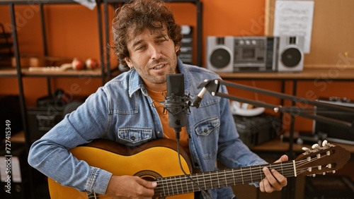 A handsome hispanic man recording music in a studio while playing an acoustic guitar.