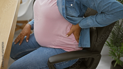 Young hispanic woman suffering backache at work, pregnant business worker battles spinal pain in the office