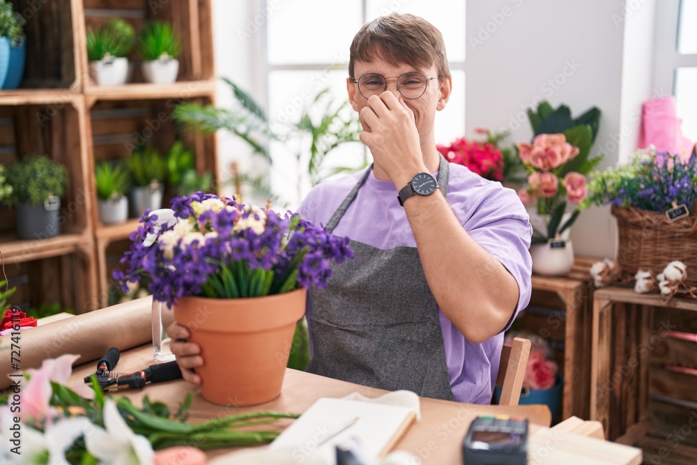 Caucasian blond man working at florist shop smelling something stinky and disgusting, intolerable smell, holding breath with fingers on nose. bad smell
